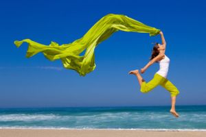 Beautiful young woman jumping on  the beach with a colored tissue